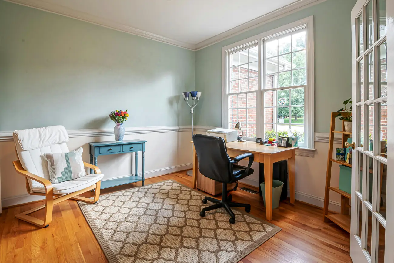 A bright, organized home office workspace with a wooden desk, black office chair, and a view of a window.