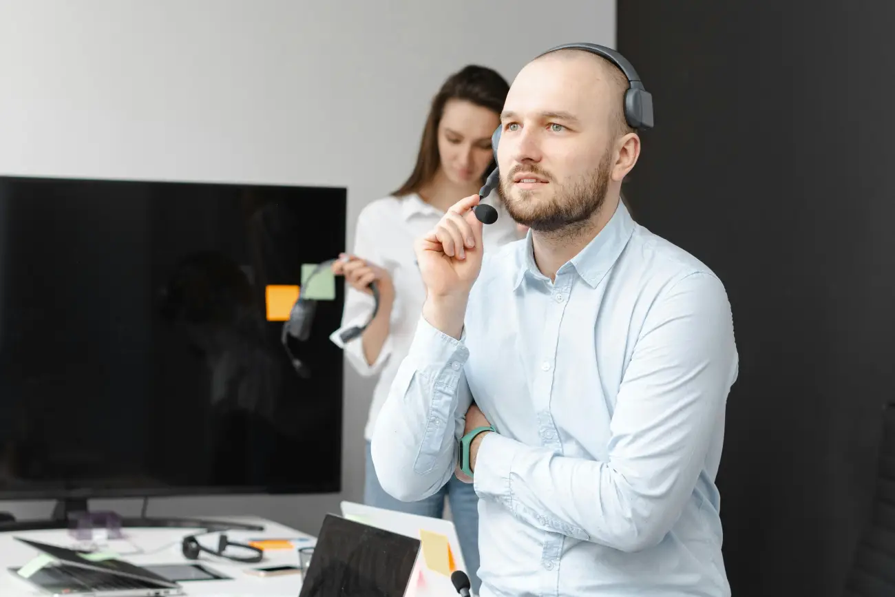 A focused e-commerce customer service agent wearing a headset, with a colleague in the background.