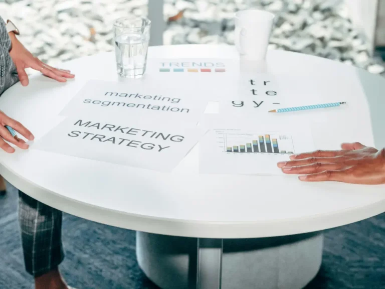 Marketing documents with "MARKETING STRATEGY" and "segmentation" written on them lay on a white meeting table.