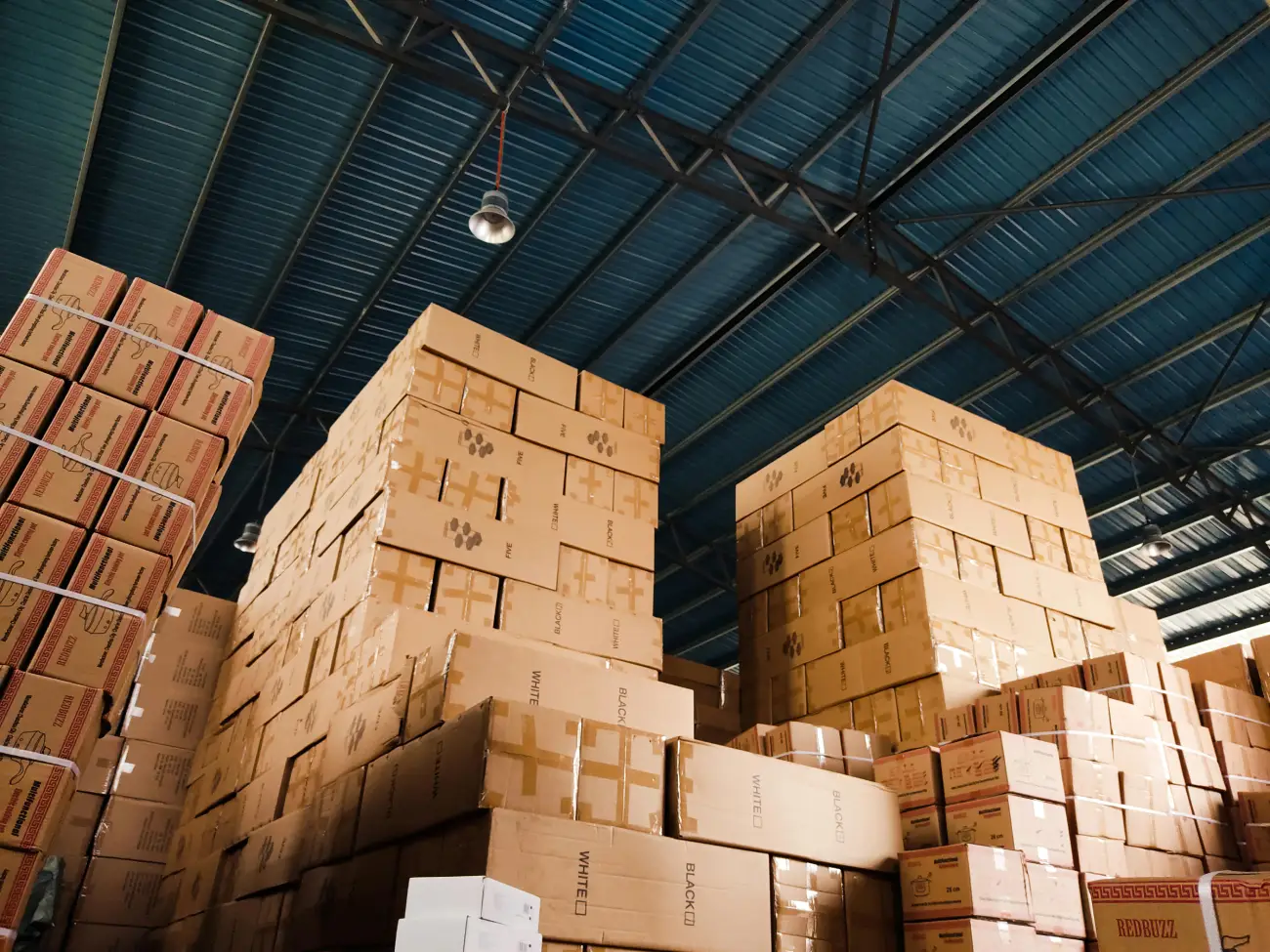 High stacks of brown shipping boxes in a large e-commerce logistics warehouse, ready for distribution.