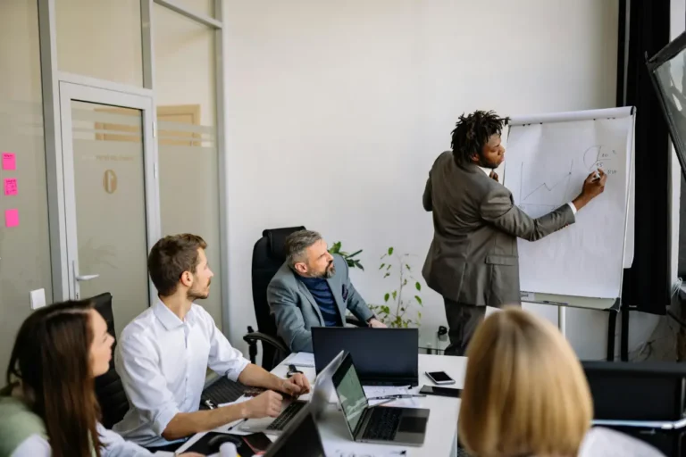 A professional team meeting in a well-lit office, with a speaker at a flipchart explaining growth metrics.