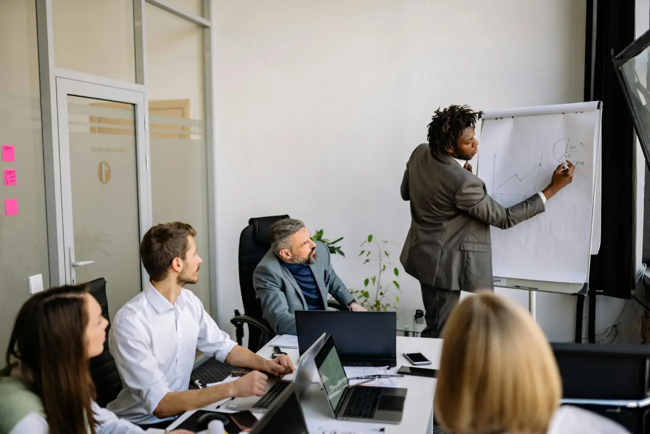 A professional team meeting in a well-lit office, with a speaker at a flipchart explaining growth metrics.